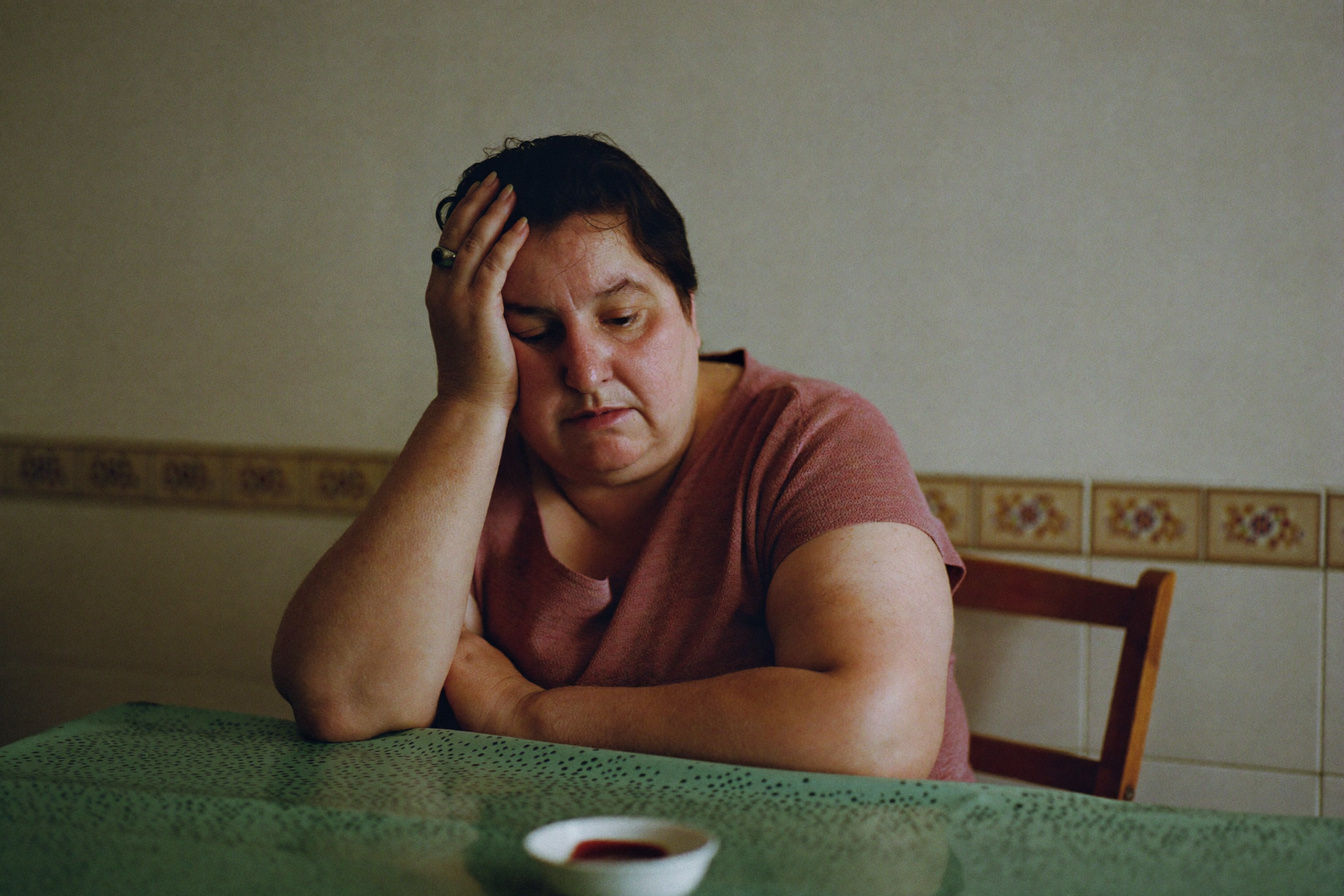 Mujer sentada a la mesa de su cocina, con la cabeza apoyada en la mano.